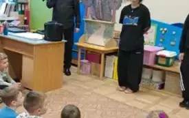 Dzieci siedzą. Przed nimi stoi tancerka ubrana na czarno.
