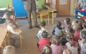 Leśnik stoi przed dziećmi. Dzieci siedza na dywanie.