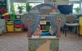 Na dywanie stoi teatrzyk. W teatrzyku są dzieci. Trzymają w rękach wykonane figurki na patyczku.