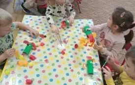 Dzieci siedza przy stolikach. Na stoliku jest cerata. Dzieci mają kolorowe rolki. Przyklejają do nich frędzelki z bibuły.