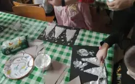 Dzieci siedzą przy stoliku. Wykonują prace plastyczną.