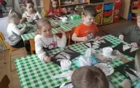 Dzieci siedza przy stoliku. Wykonują prace plastyczną.