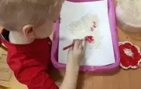 Chłopiec siedzi przy stoliku. MAluje farbami serce.