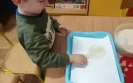 Chłopiec siedzi przy stoliku. Obssypuje serduszko ryżem.