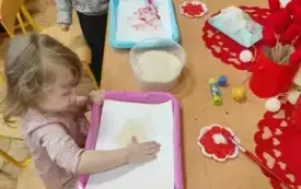 Dziewczynka i chłopiec malują farbami serce. Siedza przy stoliku.