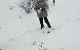 Chłopiec bawi się na śniegu. Ubrany jest w ciepłą kurtkę i czapkę.