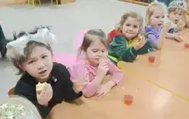 Dzieci siedzą przy stolikach i jedzą pączki.