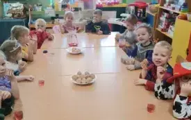 Dzieci siedzą przy stolikach jedzą pączki.