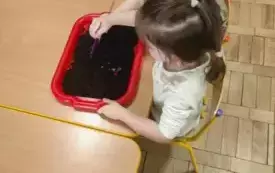 Dziewczynka rozsypuje piasek pędzelkiem.
