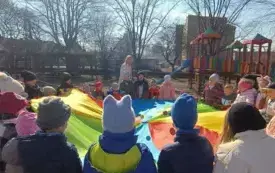 Dzieci bawią się chustą animacyjną w ogrodzie.