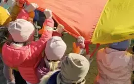 Dzieci podnoszą do g&oacute;ry kolorową chustę animacyjną.