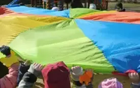 Dzieci podnoszą do g&oacute;ry kolorową chustę animacyjną.