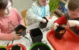 Dziewczynki nasypują ziemię do doniczek.