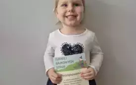 Dziewczynka trzyma w rękach podziękowanie. Uśmiecha się.
