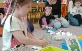 Dziewczynka wkłada odpad do zielonego kosza.