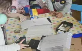 Dzieci opklejają pudełka kartonowe kolorowym papierem.