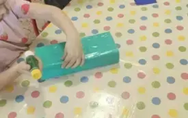 Dzieci opklejają pudełka kartonowe kolorowym papierem.