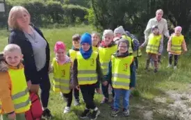 Dzieci z nauczycielką stoją w lesie.