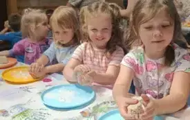 Dzieci siedza przy stoliku lepią chlebek