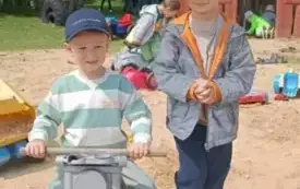 Chłopiec siedzi na motorze obok stoi drugi chłopiec