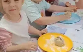 Dzieci siedzą przy stoliakch lepią chlebek