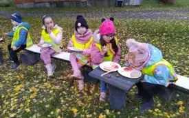 Dzieci siedzą na ławce i jedzą kiełbase.