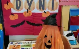 Dziecko przebrane za dynię stoi na tle napisu Dzień Dyni