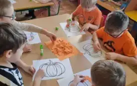 Dzieci siedzą wyklejają dynię . 
