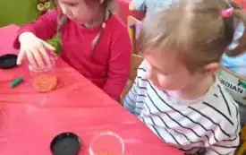 Dziewczynki wsypują pomarańczowy ryż do plastikowego pojemnika