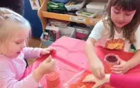 Dziewczynki wsypują pomarańczowy ryż do plastikowego pojemnika