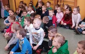 Dzieci siedzą w sali gimnastycznej w grupie
