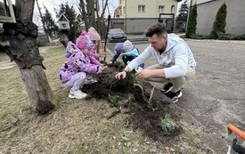 Dzieci z nauczycielem sadzą kwiaty w ogrodzie przedszkolnym.