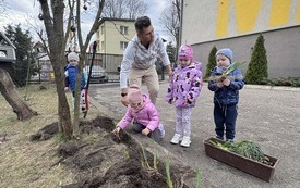 Dzieci z nauczycielem sadzą kwiaty w ogrodzie przedszkolnym.