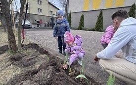 Dzieci z nauczycielem sadzą kwiaty w ogrodzie przedszkolnym.