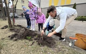 Dzieci z nauczycielem sadzą kwiaty w ogrodzie przedszkolnym.