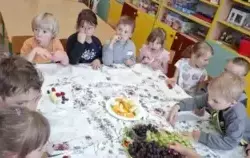 Dzieci siedzą przy stole, jedzą owoce.