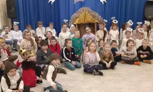 Dzieci siedzą przed szopką bożonarodzeniową 