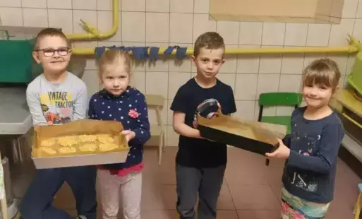 Dzieci trzymają ciasteczka owsiane ,aby kucharka włożyła do pieca.