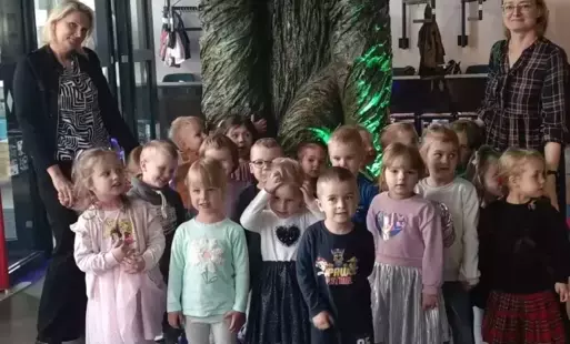 Dzieci stoją przy dużym drzewie w teatrze. Uśmiechają się do zdjęcia.