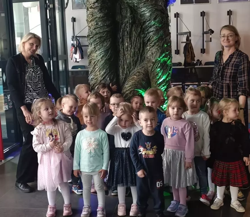 Dzieci stoją przy dużym drzewie w teatrze. Uśmiechają się do zdjęcia.