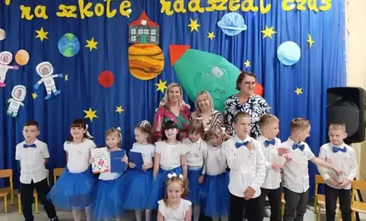 Dzieci stoją wraz z nauczycielami ,uśmiechają się .