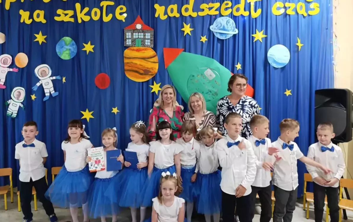 Dzieci stoją wraz z nauczycielami ,uśmiechają się .