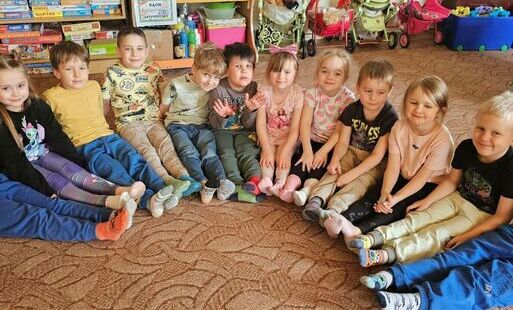 Dzieci siedza na dywanie i pokazują kolorowe skarpetki
