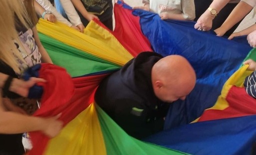 Dzieci wraz z rodzicami biorą udział w zabawie ruchowej . 