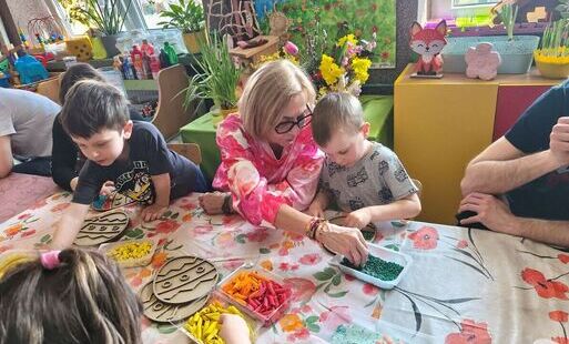 Dzieci z rodzicami siedzą przy stoliku wykonują pracę.