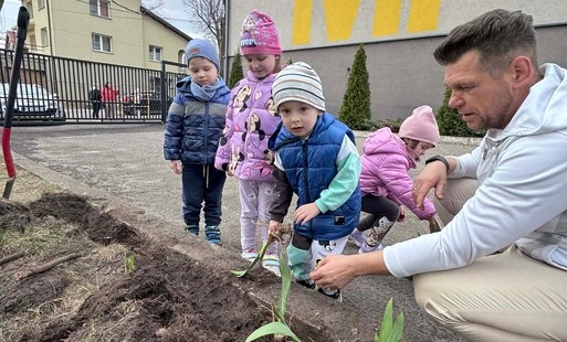 Dzieci z nauczycielem sadzą kwiaty w ogrodzie przedszkolnym.